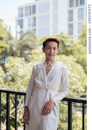 Vertical portrait of non-binary gay Thai man leaning on balcony railing outdoors 140345472