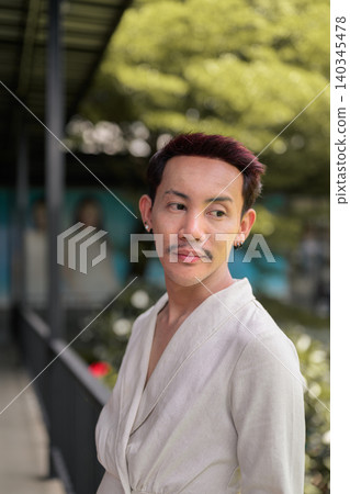 Vertical close up portrait of non-binary gay Thai man looking away on covered outdoor walkway 140345478