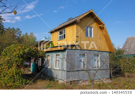 A small wooden village country house with a triangular roof. An old hut with a garden plot. A small wooden village country house with a triangular roof. An old hut with a garden plot. 140345559