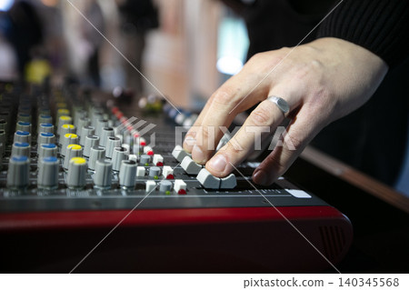 Sound technician adjusting audio levels on mixing console during an event at a convention center Sound technician adjusting audio levels on mixing console during an event at a convention center 140345568