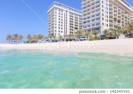 Luxurious beachfront resort setting on a sunny day with pristine waters and palm trees in clear view Luxurious beachfront resort setting on a sunny day with pristine waters and palm trees in clear view 140345591