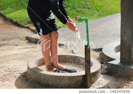 Unrecognizable child in swimwear washing hands under an outdoor public water tap after the beach. Summer vacation holiday lifestyle, cleaning up at a shower station outdoors with splashing water. Unrecognizable child in swimwear washing hands under an outdoor public water tap after the beach. Summer vacation holiday lifestyle, cleaning up at a shower station outdoors with splashing water. 140345646