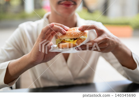 Close Up of Cheeseburger Held by Person at Outdoor Cafe Close Up of Cheeseburger Held by Person at Outdoor Cafe 140345690