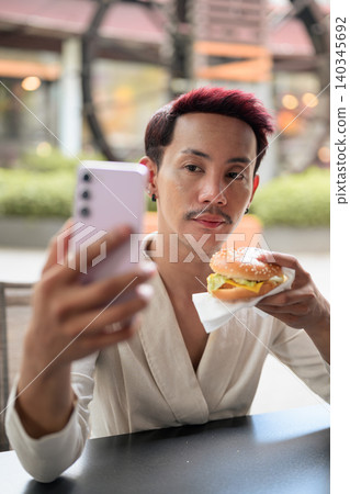 Thai Non-Binary Gay Man Taking Selfie with Burger Outdoors Thai Non-Binary Gay Man Taking Selfie with Burger Outdoors 140345692