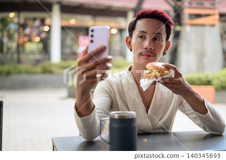 Thai Non-Binary Gay Man Taking Selfie with Burger Outdoors 140345693