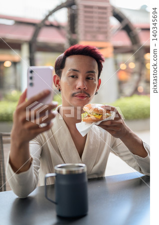 Thai Non-Binary Gay Man Vertical Portrait Vlogging with Burger and Coffee Thai Non-Binary Gay Man Vertical Portrait Vlogging with Burger and Coffee 140345694