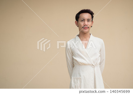 Thai Non-Binary Gay Man Posing with Hands Behind Back against Plain Wall Thai Non-Binary Gay Man Posing with Hands Behind Back against Plain Wall 140345699
