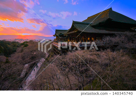 A beautiful sunset sinks into the Kyoto cityscape and the stage of Kiyomizu-dera Temple at closing time in winter [Kyoto Tower in the distance]. 140345740
