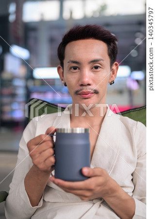 Thai Non-Binary Gay Man Using Smartphone and Holding Coffee Mug Landscape Thai Non-Binary Gay Man Using Smartphone and Holding Coffee Mug Landscape 140345797