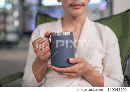 Close Up of Blue Thermal Travel Mug Held by Person Landscape 140345801