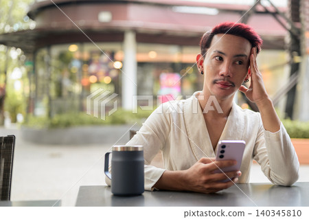 Thai Non-Binary Gay Man Thinking and Holding Smartphone Outside Cafe Thai Non-Binary Gay Man Thinking and Holding Smartphone Outside Cafe 140345810