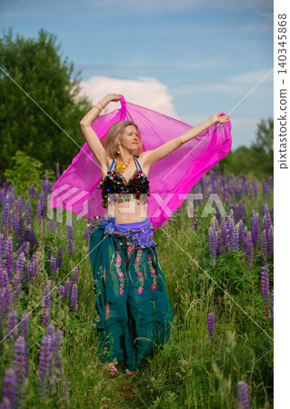 Woman dancing in a colorful outfit with a pink veil in a vibrant field of flowers Woman dancing in a colorful outfit with a pink veil in a vibrant field of flowers 140345868