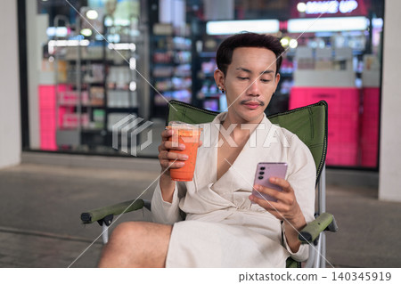 Thai Non-Binary Gay Man Texting and Drinking Iced Tea Outdoors Thai Non-Binary Gay Man Texting and Drinking Iced Tea Outdoors 140345919