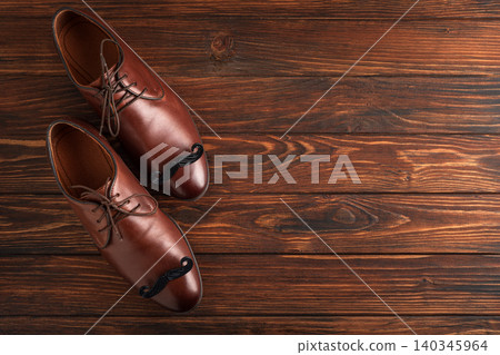 Brown leather shoes with mustaches on wooden background Brown leather shoes with mustaches on wooden background 140345964