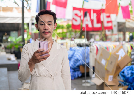 Thai Non-Binary Gay Man Using Smartphone at Street Market Sale Thai Non-Binary Gay Man Using Smartphone at Street Market Sale 140346071