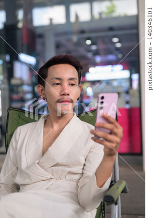 Thai Non-Binary Gay Man Using Smartphone in Folding Chair Close Up Portrait Thai Non-Binary Gay Man Using Smartphone in Folding Chair Close Up Portrait 140346101