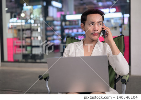 Thai Non-Binary Gay Man Multitasking with Laptop and Smartphone Call Thai Non-Binary Gay Man Multitasking with Laptop and Smartphone Call 140346104