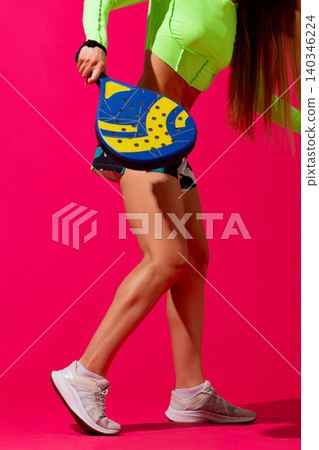 Cropped female padel player with racket on vibrant pink studio background. Cropped female padel player with racket on vibrant pink studio background. 140346224