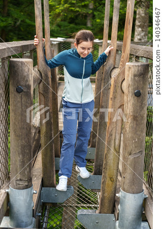 Girl walking through wooden obstacle at treetop adventure park 140346467