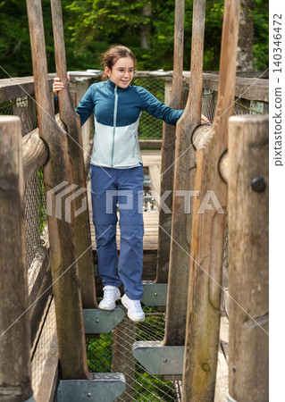 Girl walking through wooden obstacle at treetop adventure park 140346472