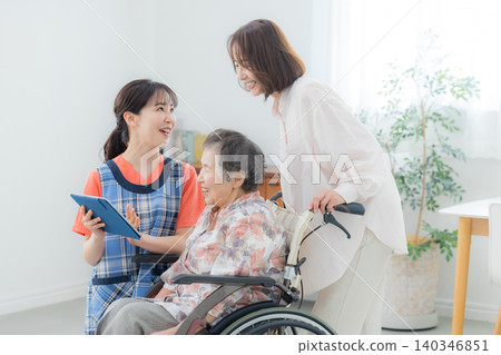 一位護理人員正在使用平板電腦，一位老人坐在輪椅上。 140346851