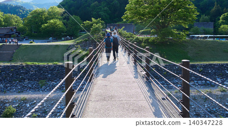 A scene of many tourists crossing the Encounter Bridge in Shirakawa-go, a popular spring tourist spot. 140347228