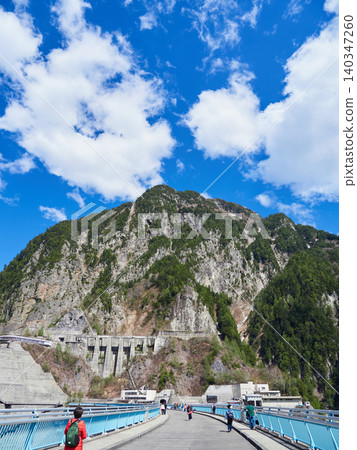Tourists crossing the Kurobe Dam on the Tateyama Kurobe Alpine Route, a popular spring tourist spot, and the mountain scenery. 140347260