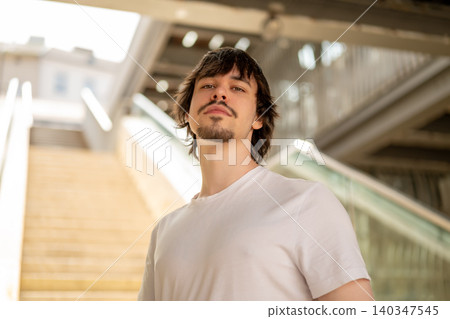 Young 25 year old man stands on a staircase among modern urban architecture. Young 25 year old man stands on a staircase among modern urban architecture. 140347545