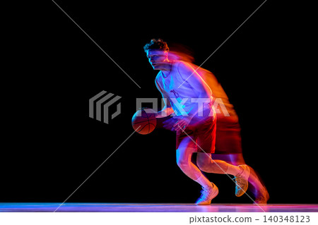 Basketball player accelerating with ball and neon trails in dark studio. Basketball player accelerating with ball and neon trails in dark studio. 140348123