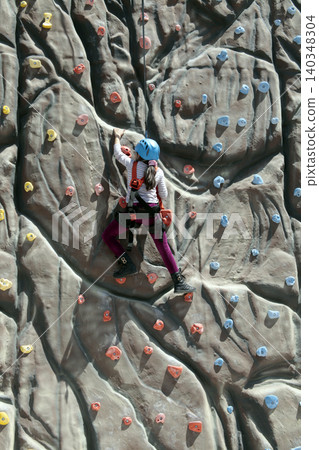 girl climbs a big rock wall at the gym girl climbs a big rock wall at the gym 140348304