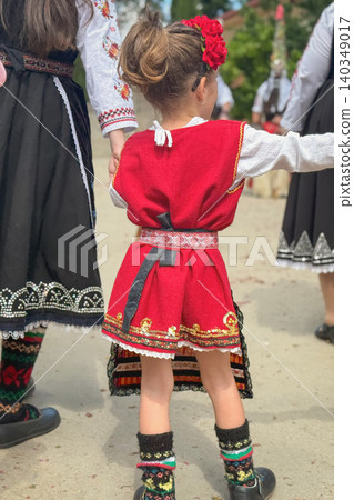 Child girl in red Bulgarian folk costume dances during Kazanlak Rose Festival, seen from back among performers. Child scene shows heritage, tradition, community, cultural festival Child girl in red Bulgarian folk costume dances during Kazanlak Rose Festival, seen from back among performers. Child scene shows heritage, tradition, community, cultural festival 140349017