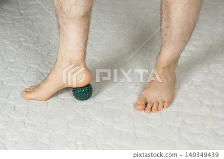 Man massaging myofascial trigger points on foot with green spiky ball Man massaging myofascial trigger points on foot with green spiky ball 140349439