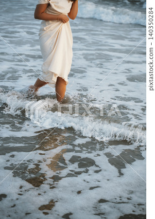 Woman Strolling Through Ocean Waves in Flowing Dress Woman Strolling Through Ocean Waves in Flowing Dress 140350284