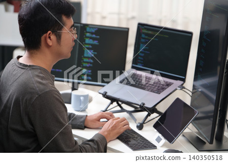 Focused Programmer Working on Multiple Screens with Code in an Office Setting Focused Programmer Working on Multiple Screens with Code in an Office Setting 140350518