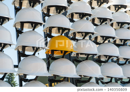 Yellow Hard Hat Standing out from Rows of White Helmets on a Rack 140350809
