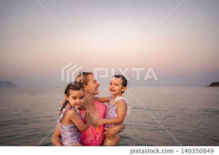 Happy mother standing in ocean with young daughters Happy mother standing in ocean with young daughters 140350849