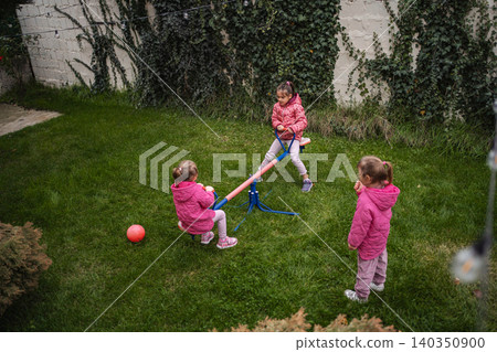 Three young girls playing on seesaw in backyard Three young girls playing on seesaw in backyard 140350900