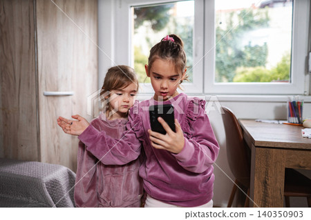 Little sisters looking at smartphone together in a kids room Little sisters looking at smartphone together in a kids room 140350903