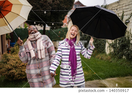 Diverse women friends laughing and holding umbrellas in rain 140350917