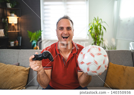 Middle age Caucasian man playing soccer video game at home Middle age Caucasian man playing soccer video game at home 140350936