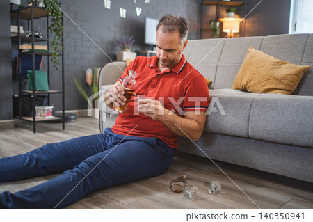 Mature man sitting on the floor and drinking alcohol Mature man sitting on the floor and drinking alcohol 140350941