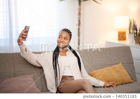 Young woman taking selfie with smartphone on sofa Young woman taking selfie with smartphone on sofa 140351183