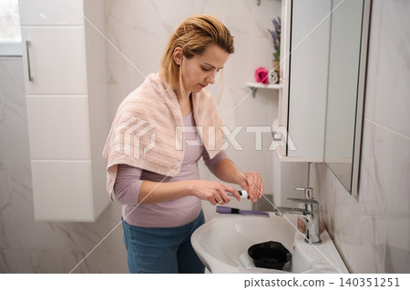 Woman preparing hair dye in bathroom sink Woman preparing hair dye in bathroom sink 140351251