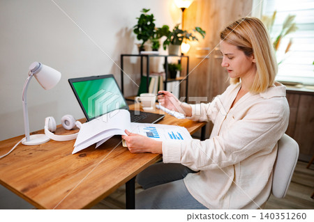 Focused individual analyzing documents while working from a cozy office space 140351260