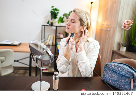 Woman applying makeup in a stylish room with natural light Woman applying makeup in a stylish room with natural light 140351467