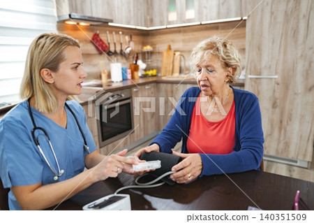 Caregiver checks blood pressure in cozy kitchen setting during afternoon visit 140351509