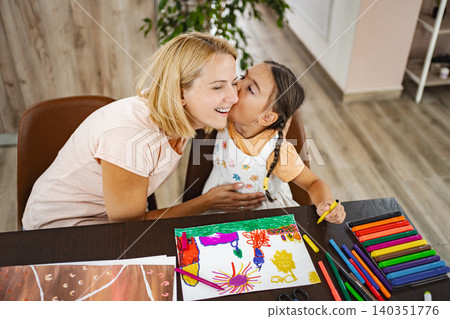 Cute girl kisses her mother while they both work on vibrant art projects Cute girl kisses her mother while they both work on vibrant art projects 140351776
