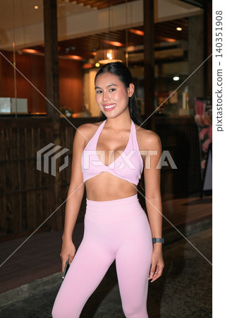 Smiling Asian woman in pink sportswear standing outside restaurant at night Smiling Asian woman in pink sportswear standing outside restaurant at night 140351908