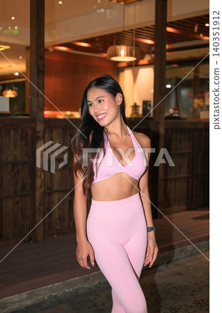Smiling Asian woman in pink sportswear looking away outside at night Smiling Asian woman in pink sportswear looking away outside at night 140351912