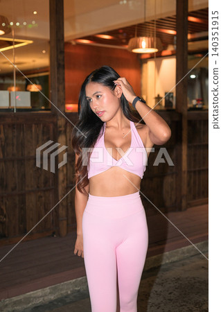 Asian woman in pink activewear touching hair outside building at night Asian woman in pink activewear touching hair outside building at night 140351915